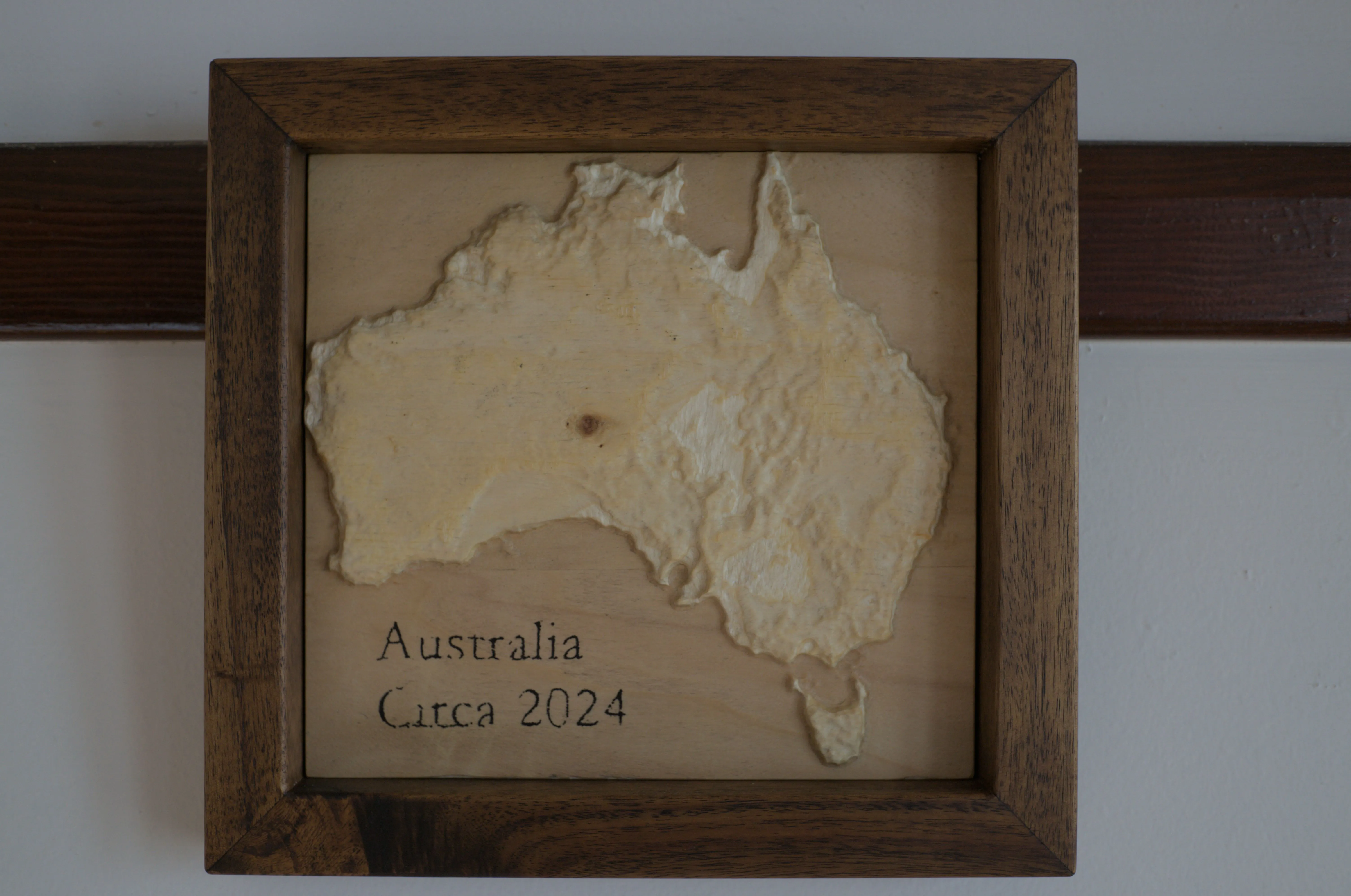 A scaled 3D Australia carved into wood and hung in a timber frame.