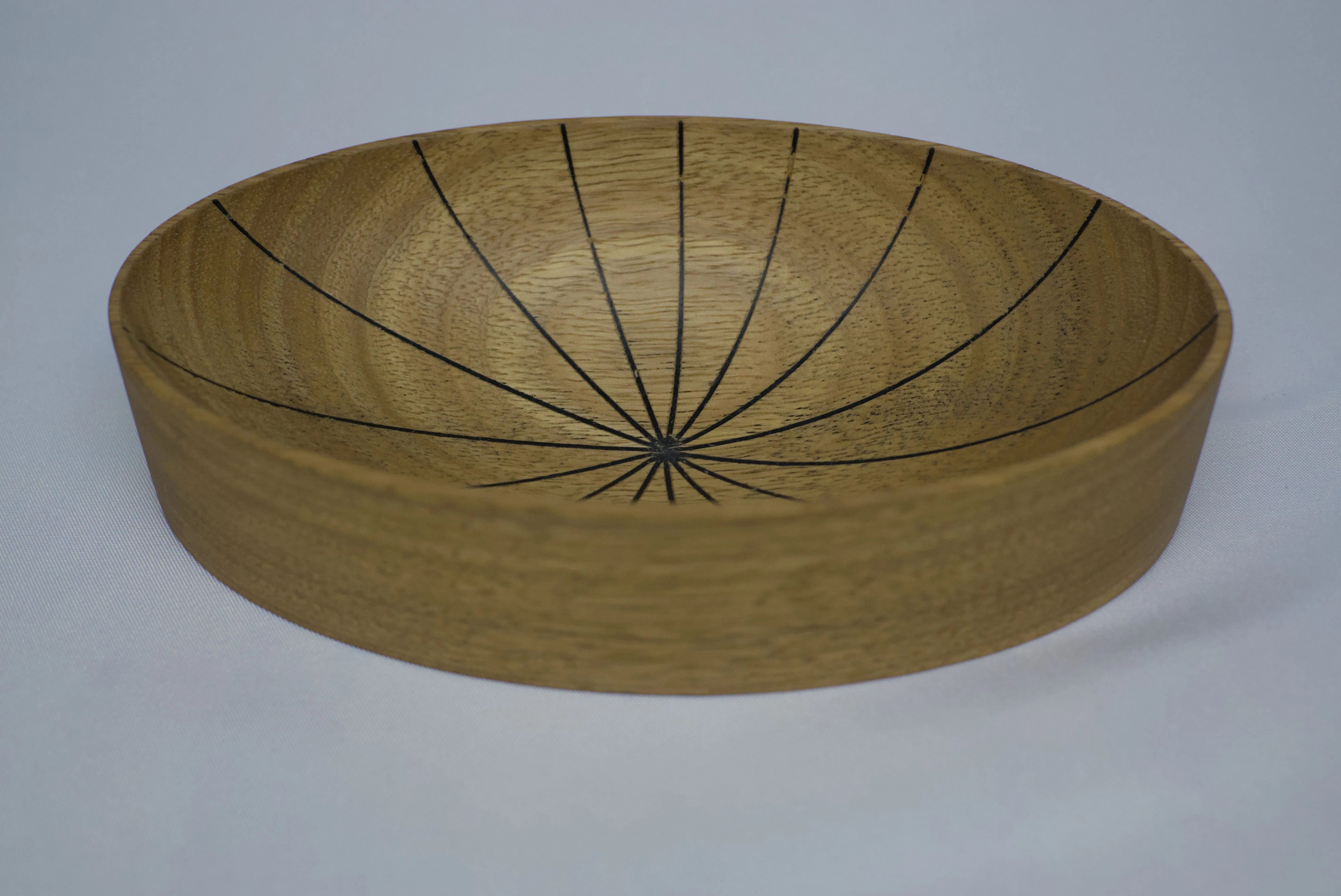 An oval shaped small bowl with numerous carved lines that meet in the center