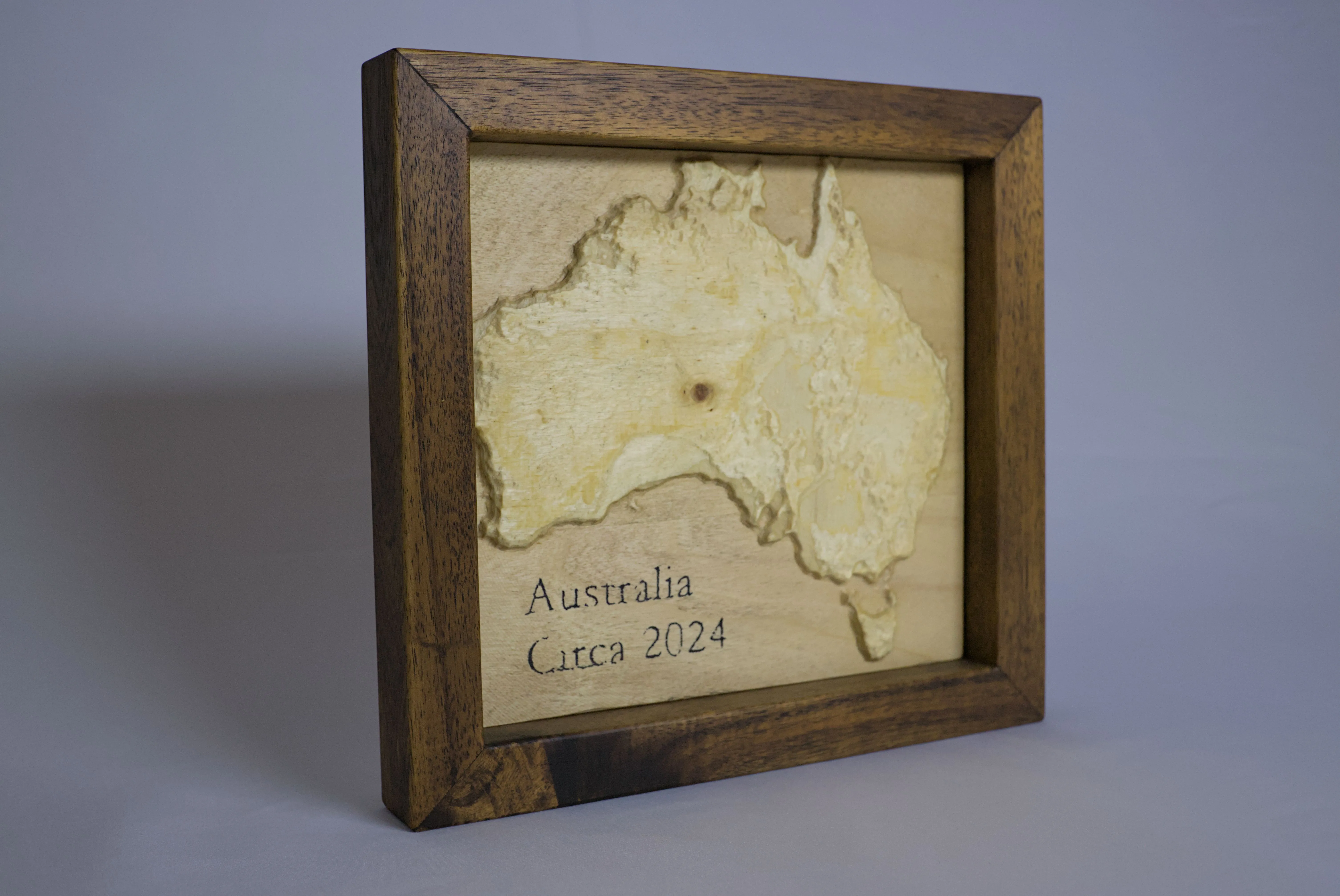Angled view of a scaled 3D Australia carved into wood and hung in a timber frame.