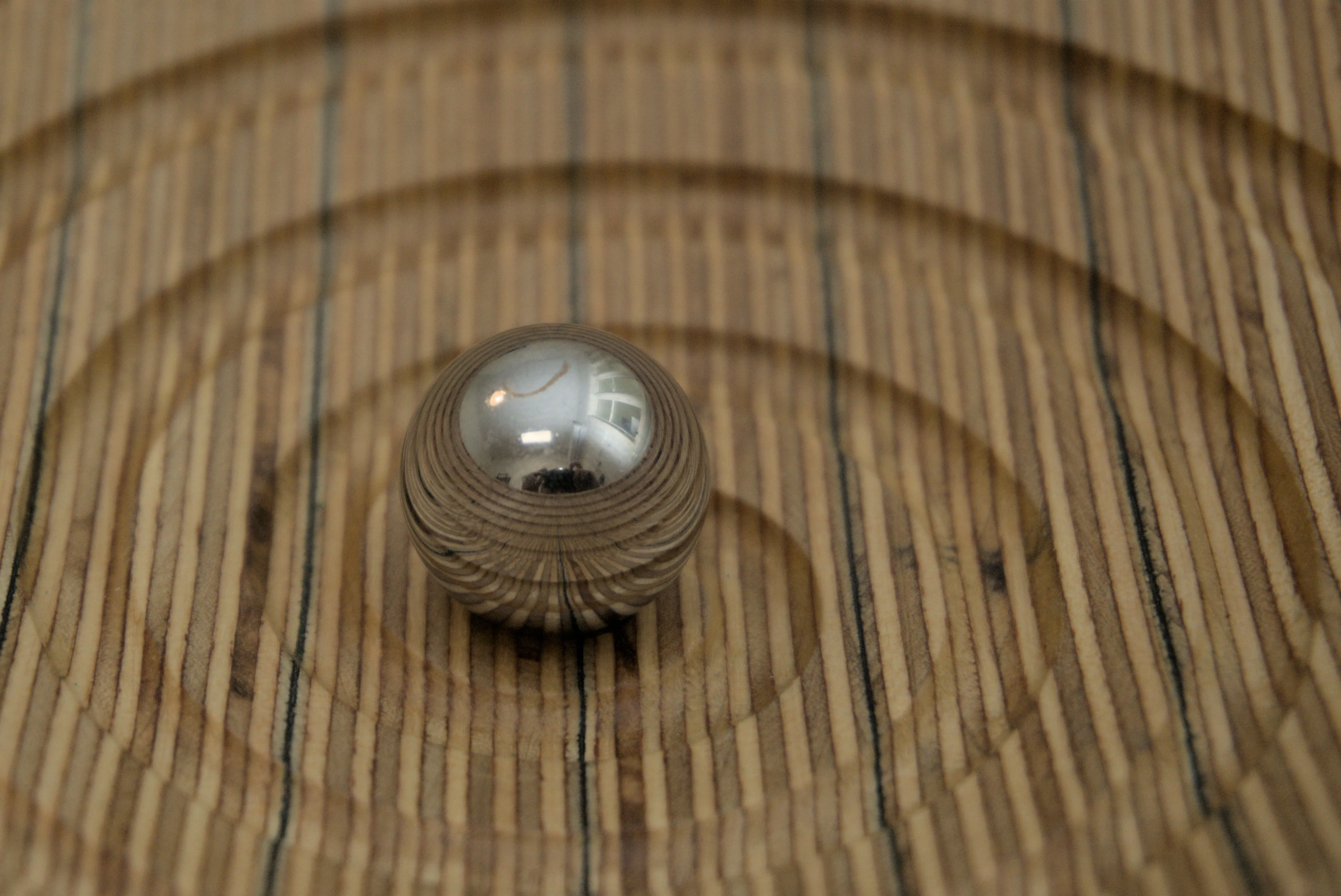 Closeup of a reflective sphere sitting in a plywood bowl with a spiralling groove