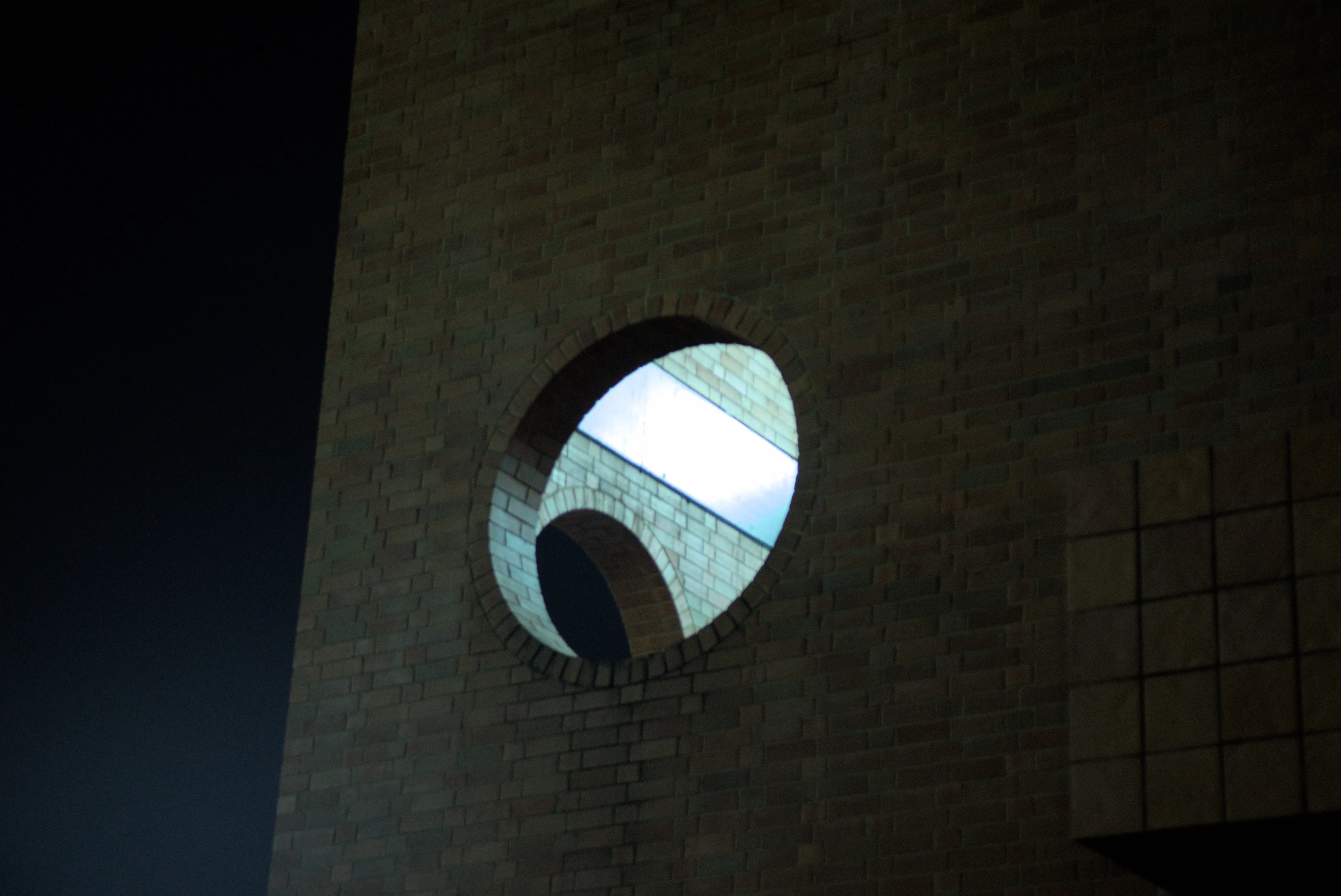 Night photo of a round opening in a brick building illuminated from the interior