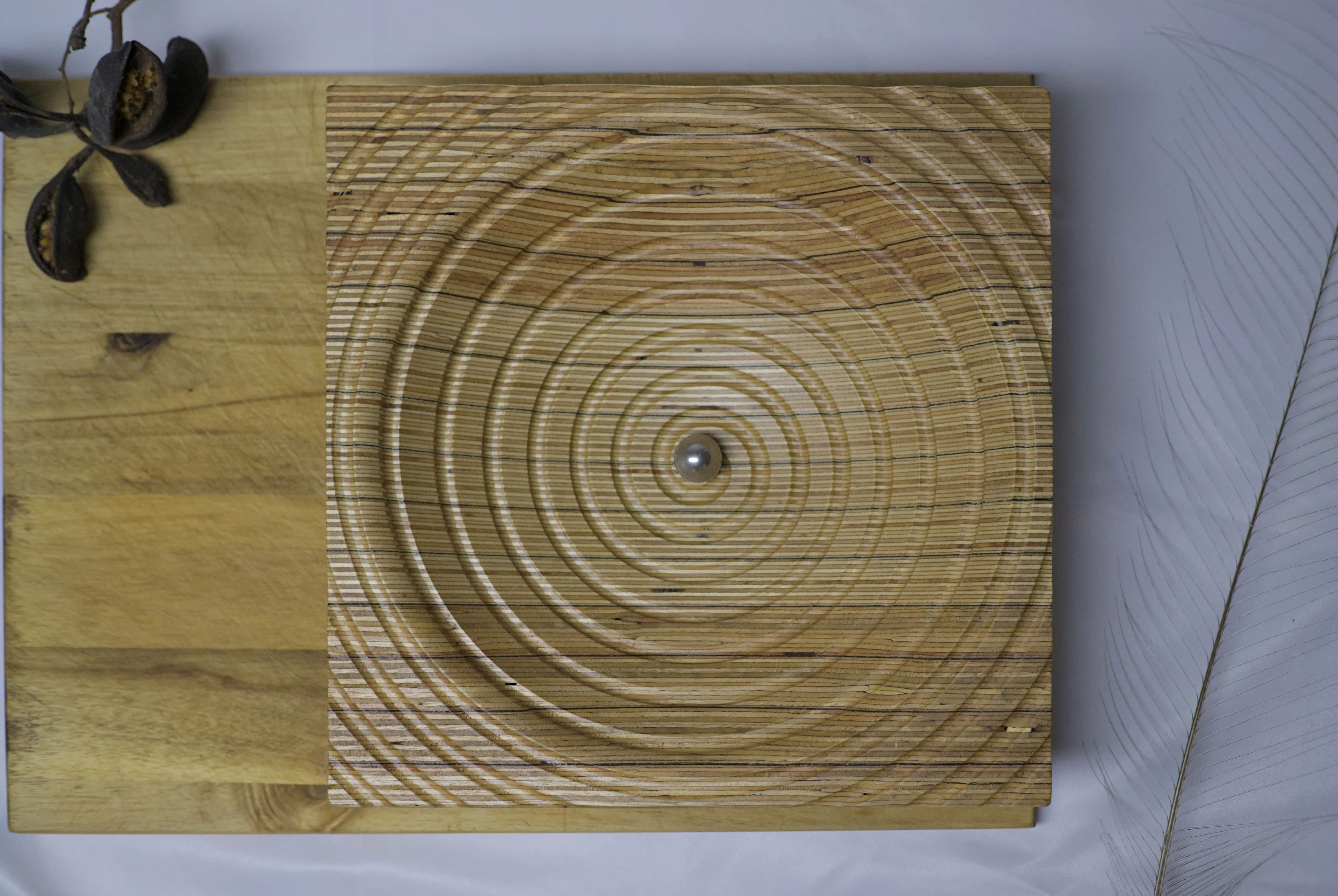 Overhead view of a plywood bowl with a groove spiralling towards the center holding a reflective sphere